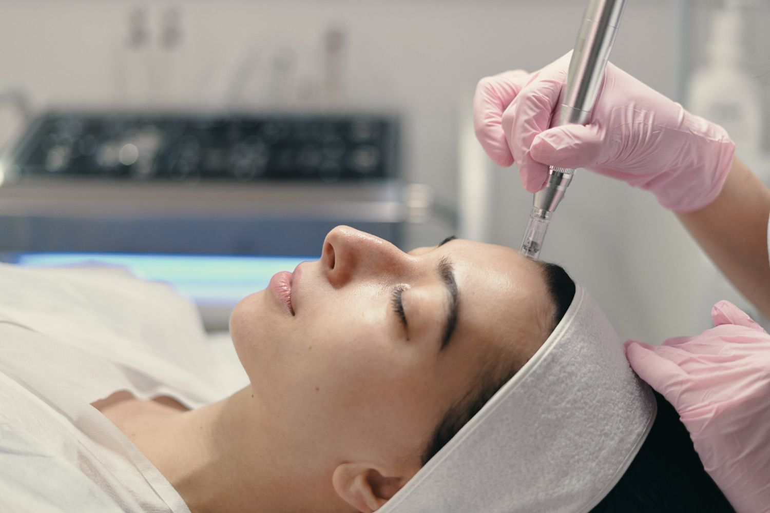 Woman receiving facial treatment, held by gloved hands, in a spa setting with closed eyes.