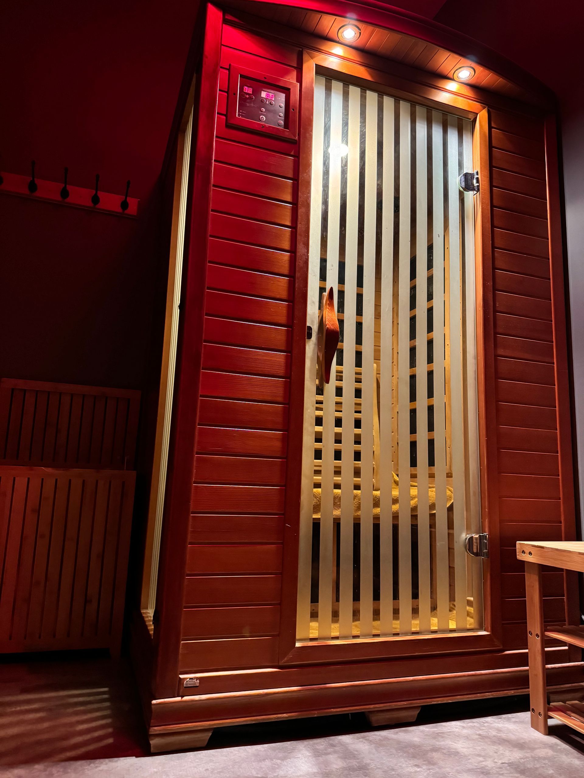 A wooden sauna with a glass door and a red ceiling.