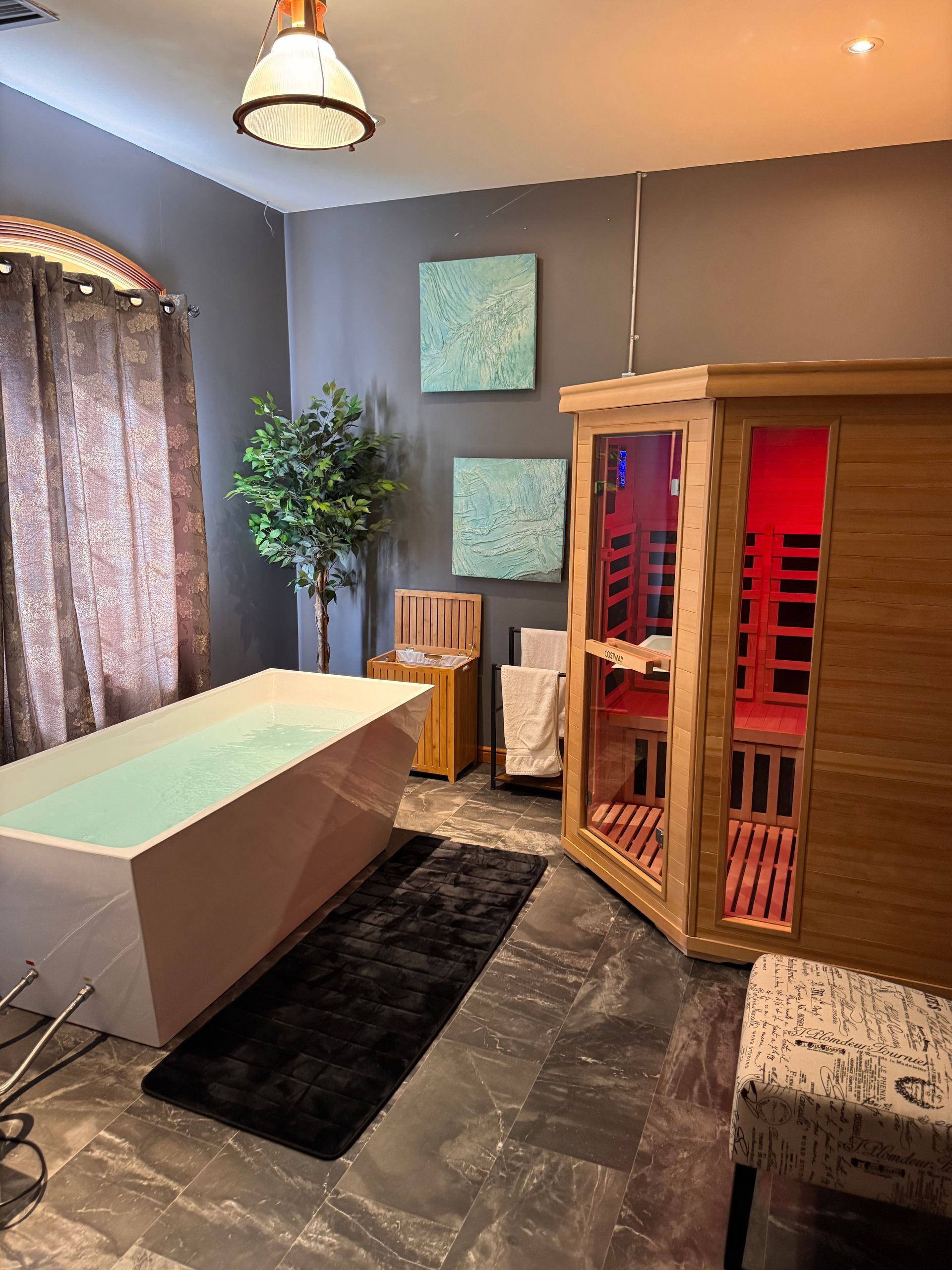 Spa room with a bathtub, sauna, artwork, and a fluffy rug.