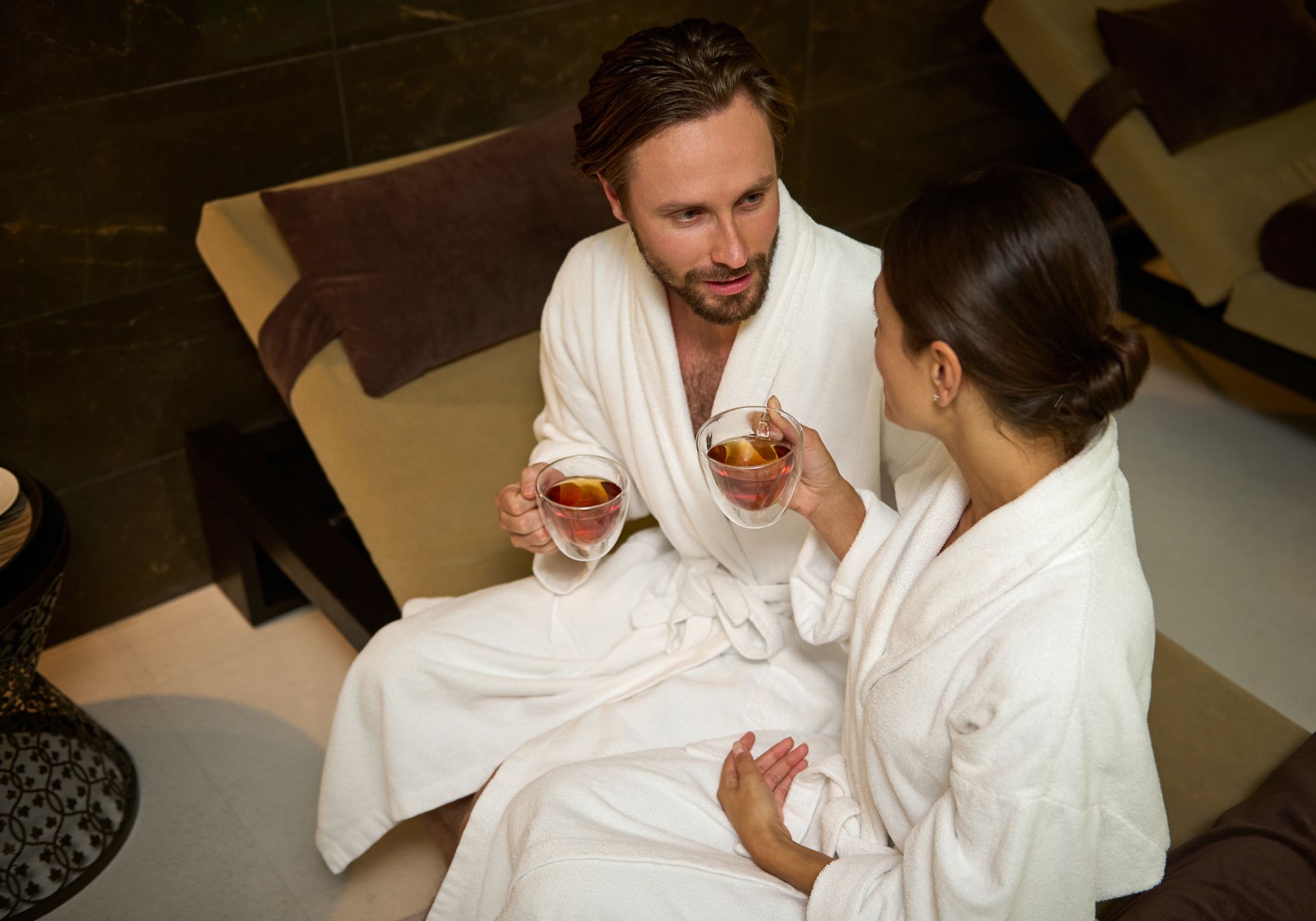 A man and a woman are sitting on a chair drinking tea.