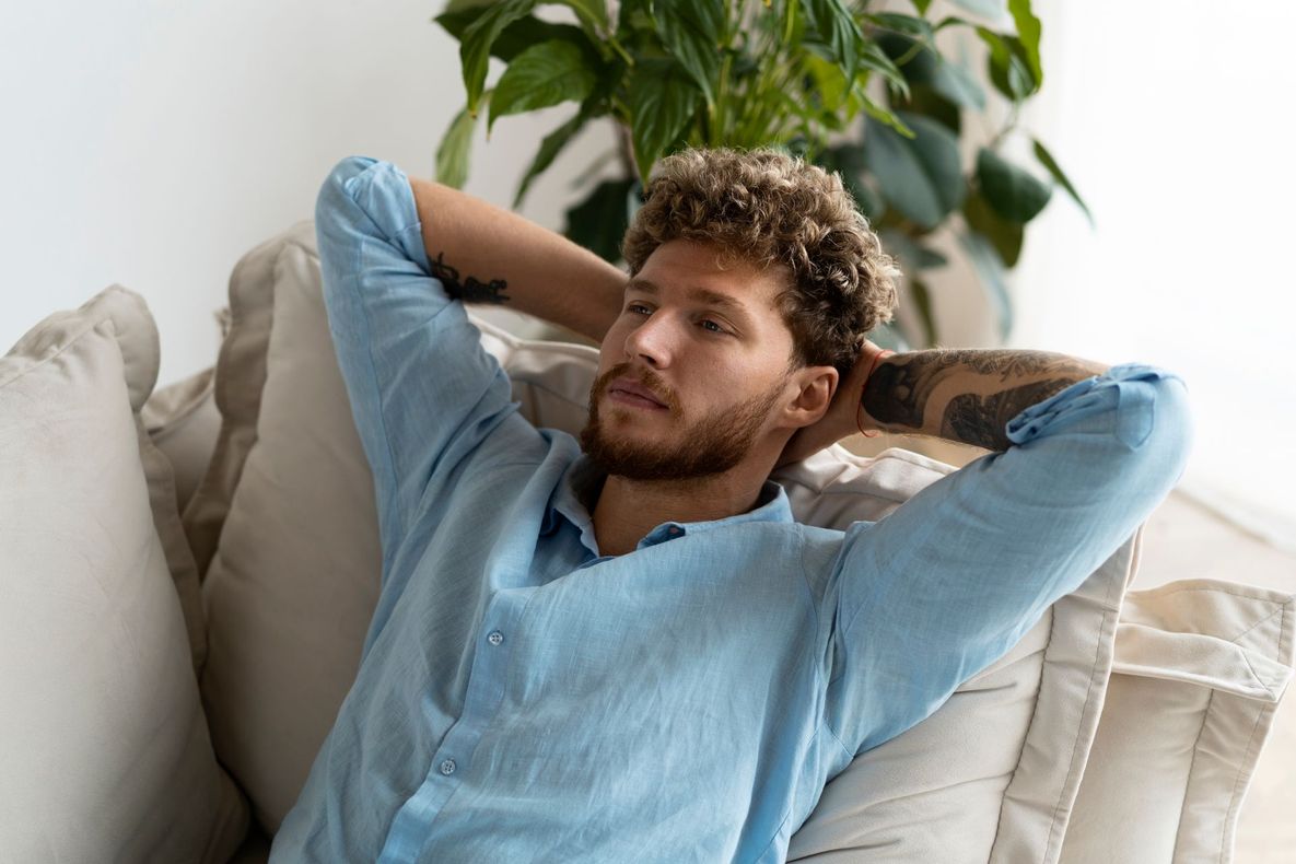 A man is sitting on a couch with his hands behind his head.