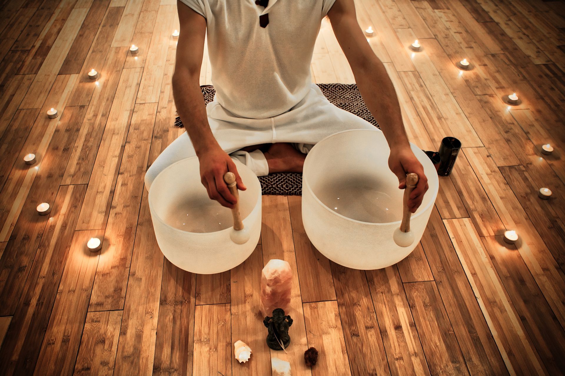 A man is sitting on the floor playing a sound bowl.