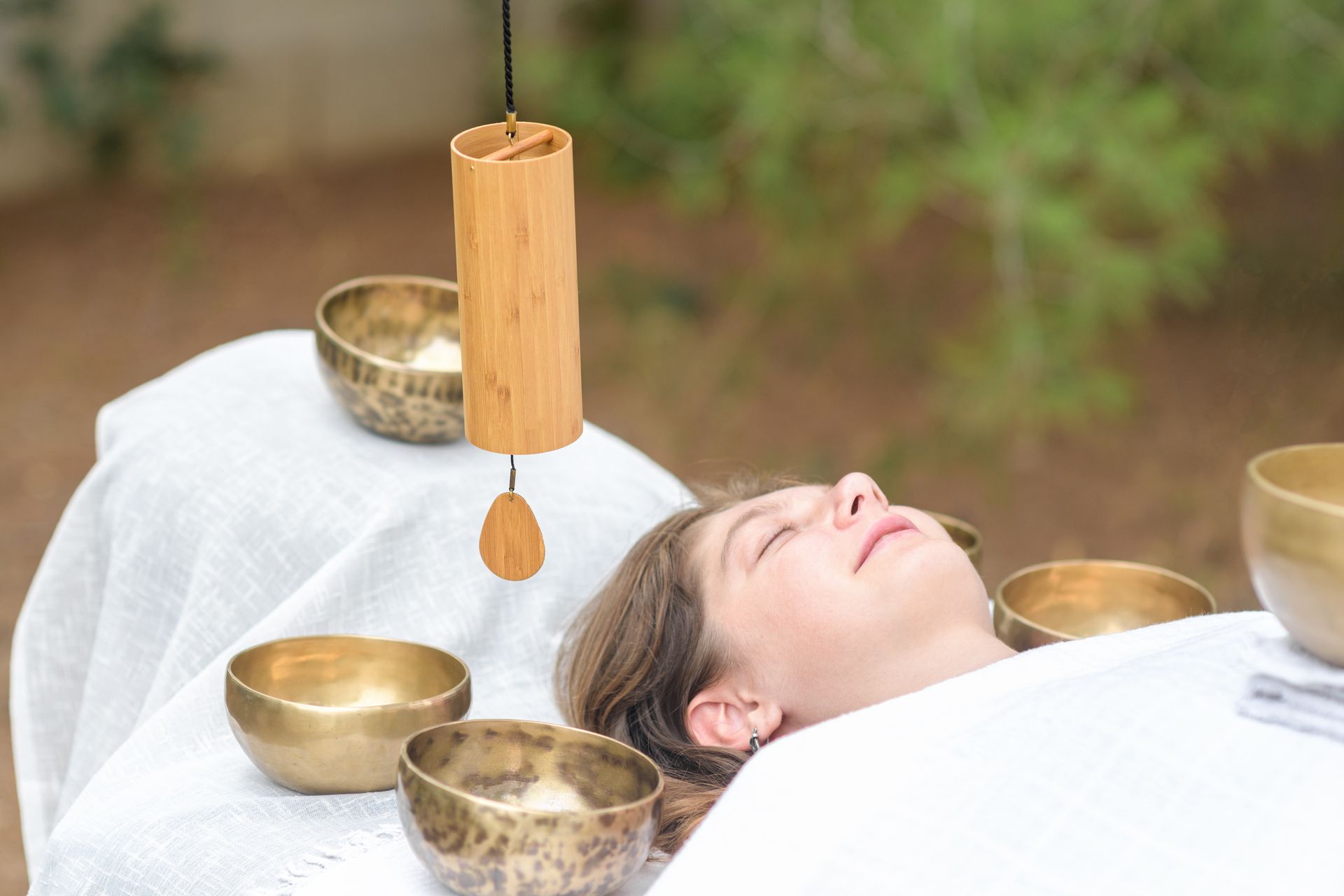 A woman is laying on a table with bowls and a chime.