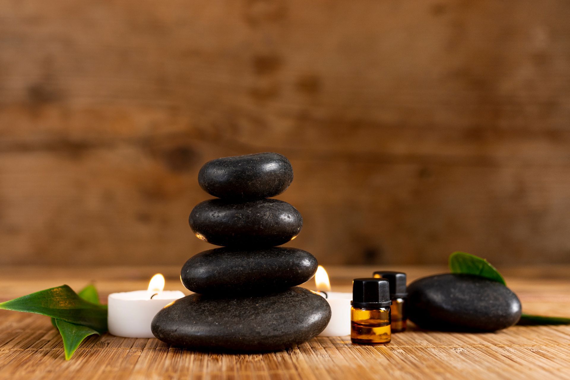 A stack of black rocks with candles and essential oils on a wooden table.