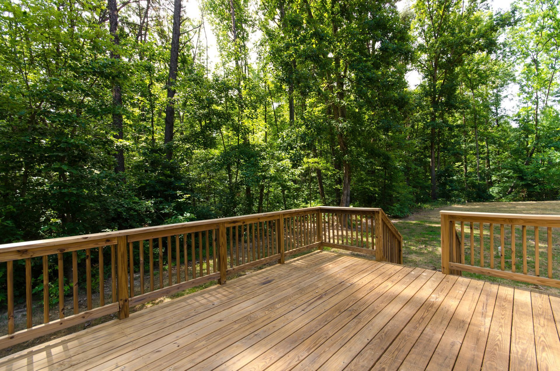 Wooden deck with railing, overlooking a lush green forest.