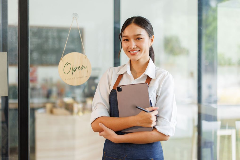 Smiling woman in apron holding tablet, standing near an 