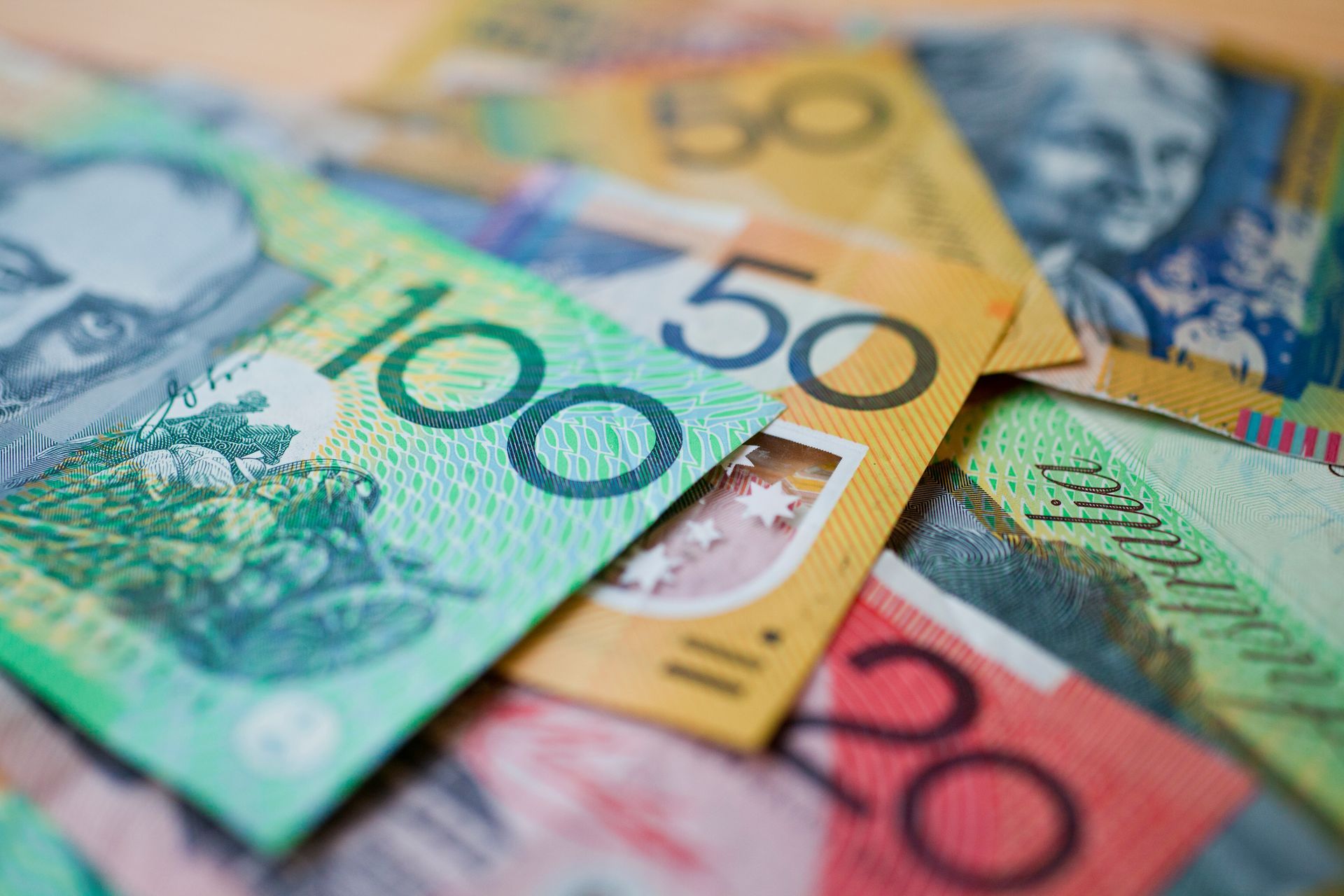 Australian banknotes: $100, $50, and $20, in green, yellow, and red, overlapping and scattered.
