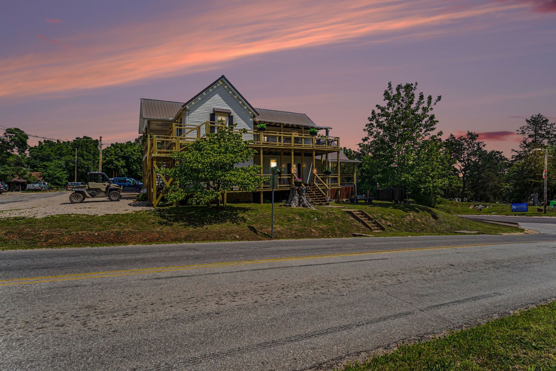 Stone house by a road at sunset, with trees and a pink-purple sky.