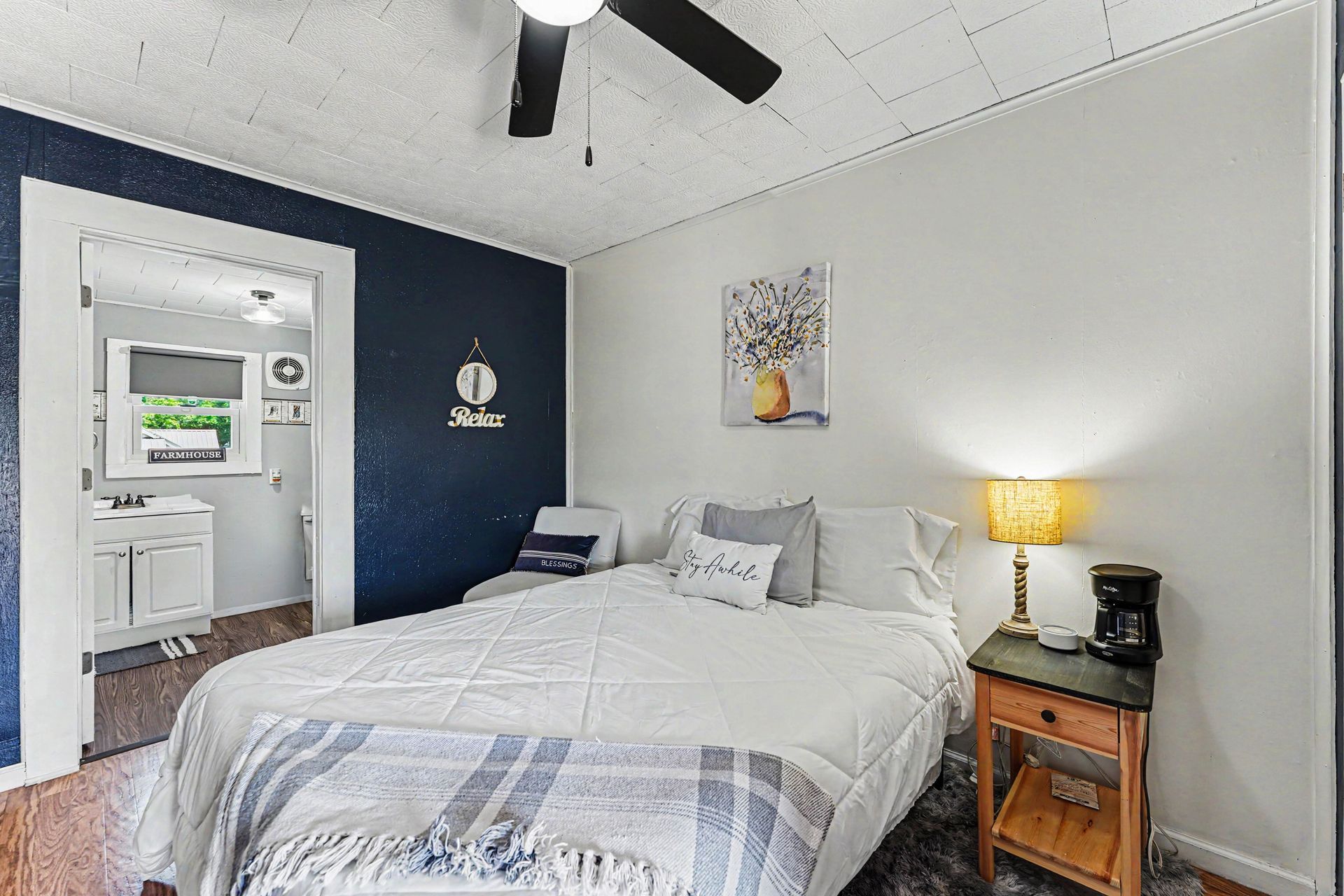 Bright bedroom with a white bed, navy accent wall, and a lit bedside lamp near a bathroom doorway.