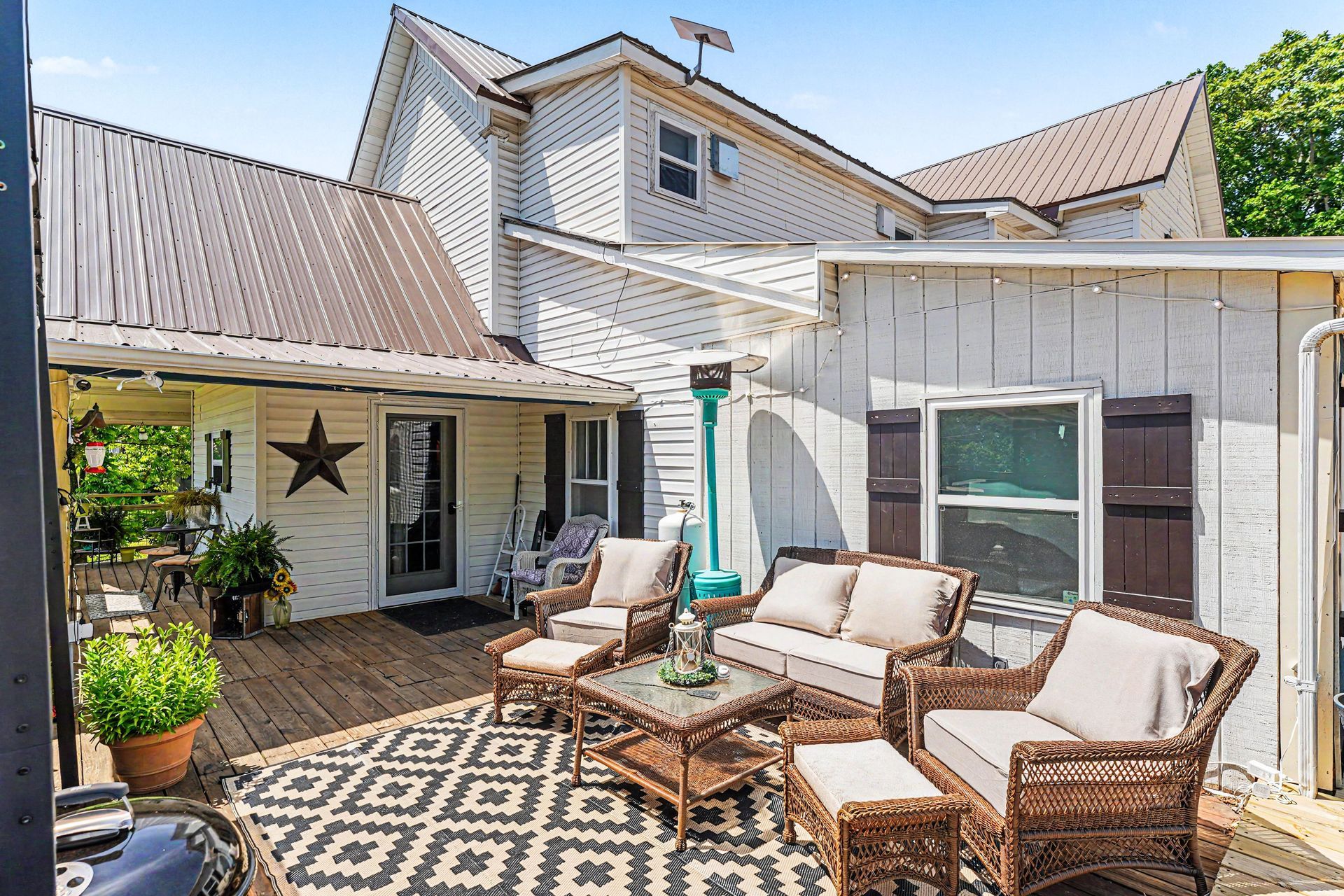 Patio with wicker seating, patterned rug, potted plants, and a white house exterior with sliding door