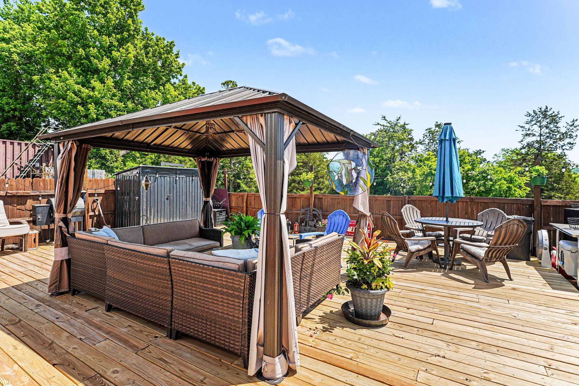 Backyard deck with gazebo, outdoor seating, grill, and blue umbrella on a sunny day