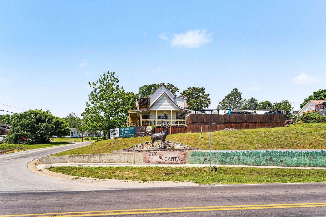 Suburban house behind a curved road and grassy hillside under a blue sky
