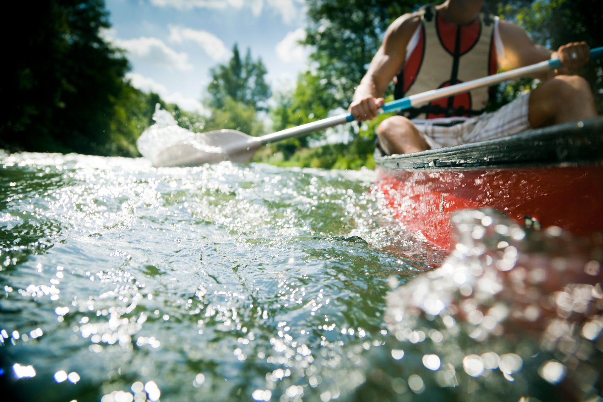 Person paddling a red canoe through choppy water in a sunny forested river