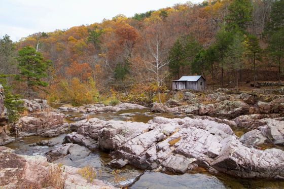 Rocky riverbed below an autumn hillside with a small cabin among trees
