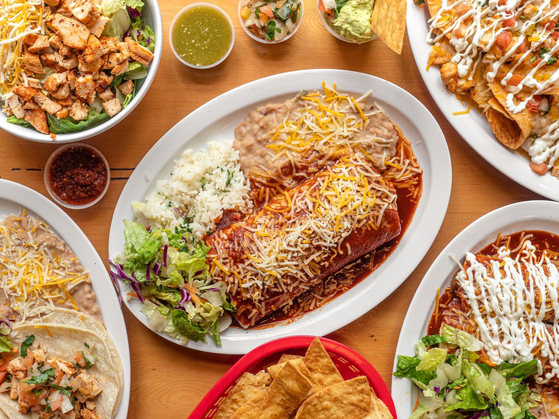Assorted Mexican dishes on a table, including enchiladas, tacos, rice, salsa, and guacamole.