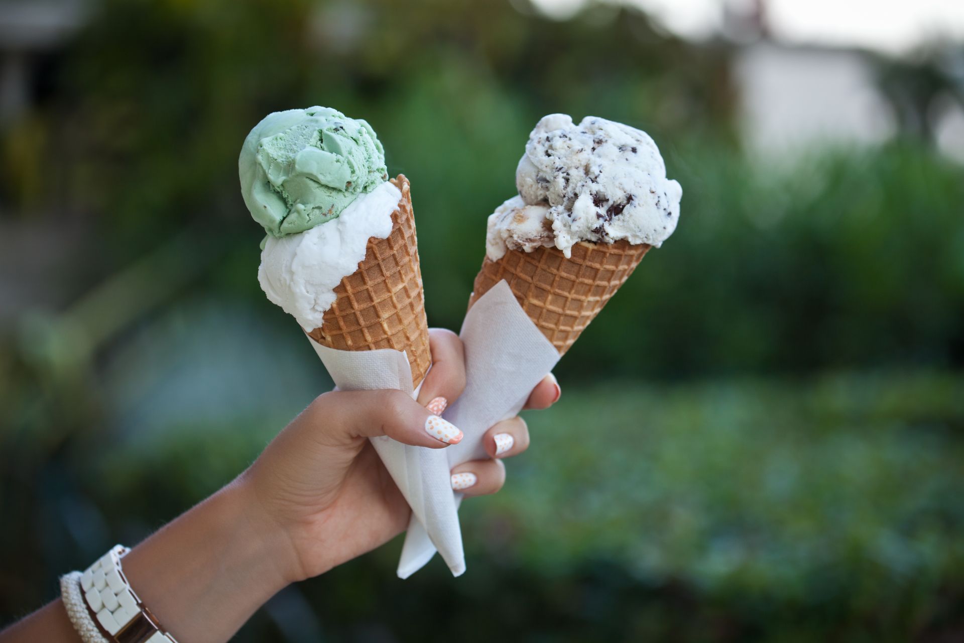 Two hands holding mint and cookies-and-cream ice cream cones outdoors