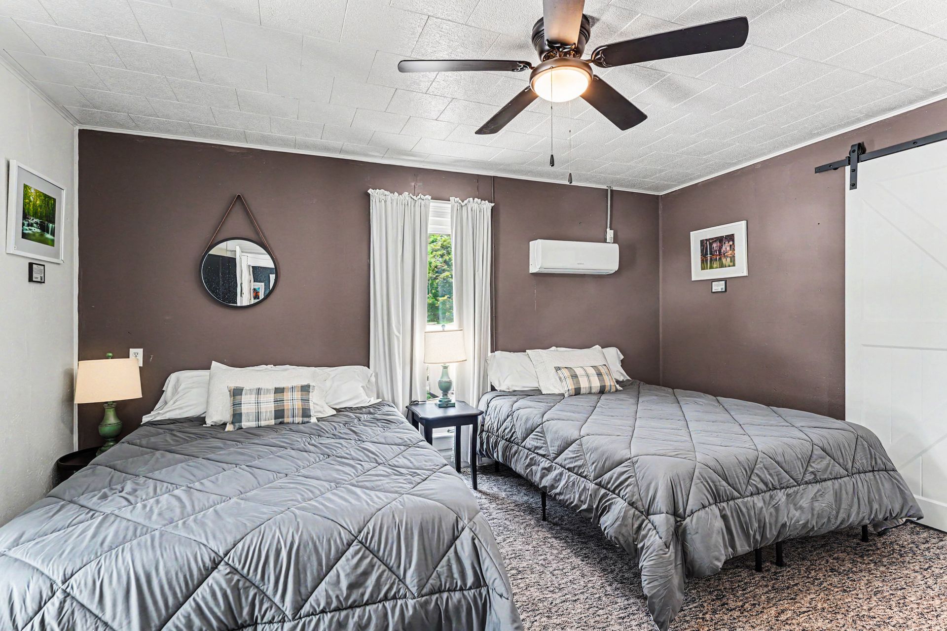 Two beds in a gray bedroom with a ceiling fan, window, and wall-mounted air conditioner