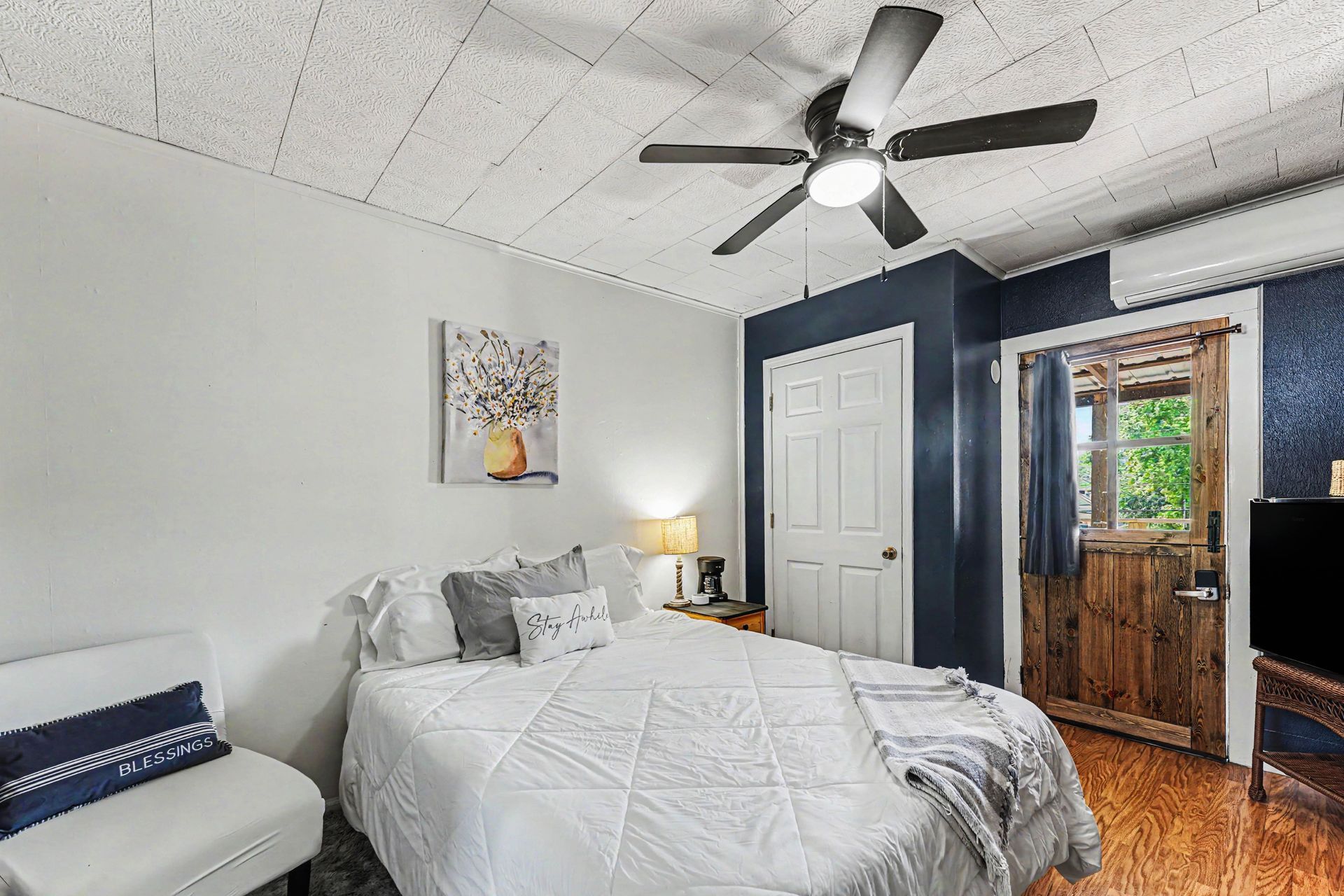 Cozy bedroom with a bed, white walls, ceiling fan, closet, and wooden door leading outside.