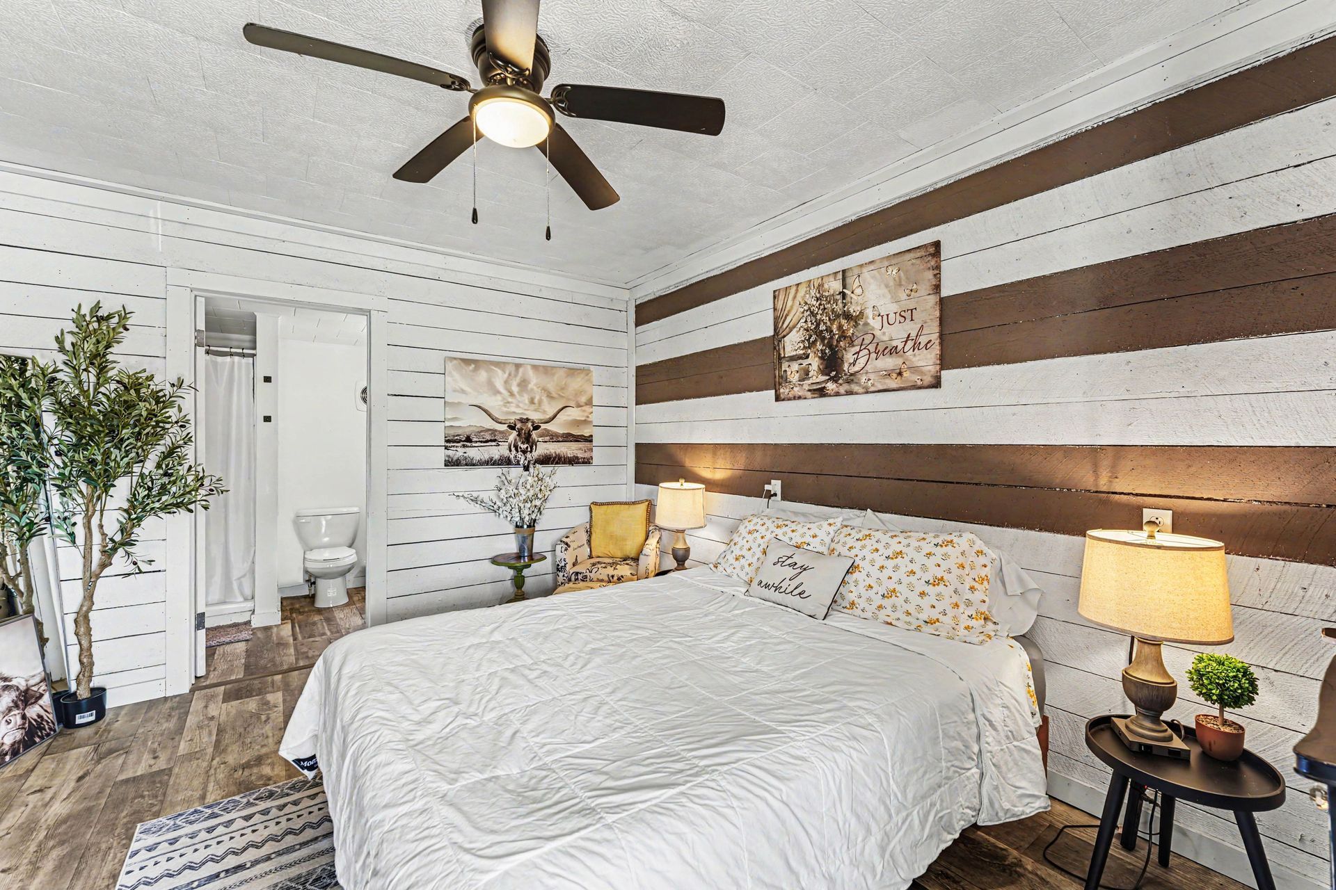 Cozy bedroom with white bed, wood-accent wall, ceiling fan, and warm bedside lamps