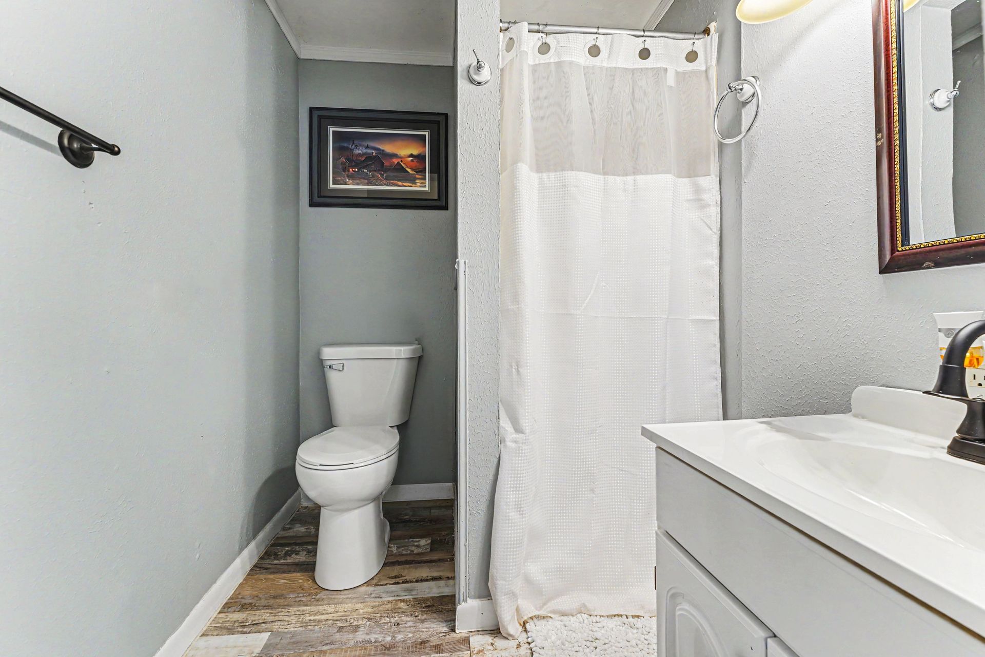 Small bathroom with toilet, shower curtain, and white vanity sink in gray walls.
