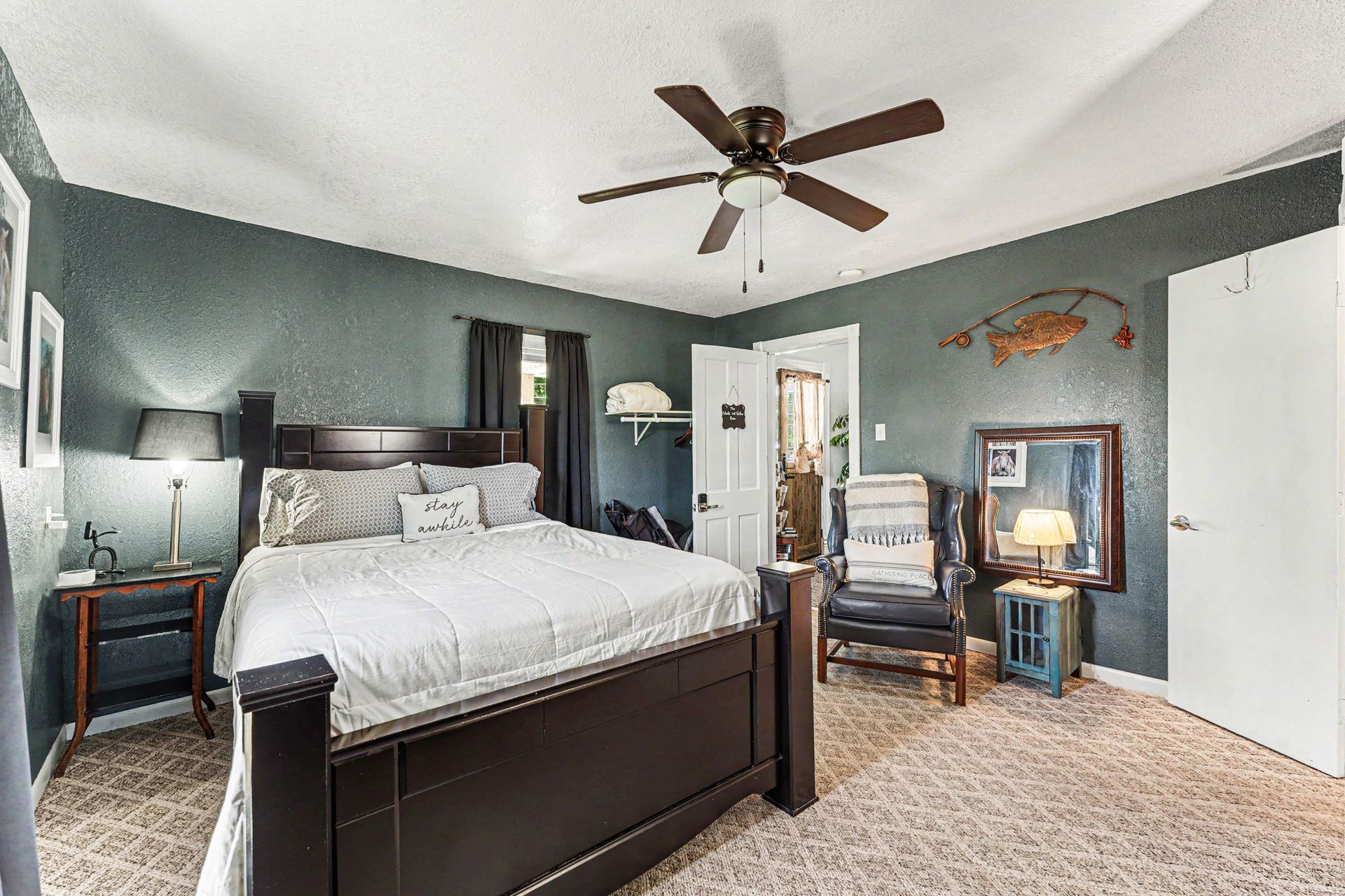 Bedroom with dark wood bed, gray walls, ceiling fan, chair, and mirrored dresser on carpeted floor