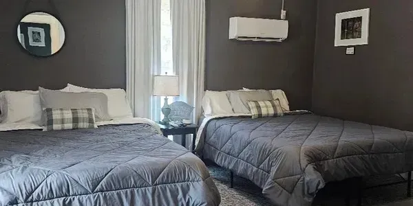Two neatly made beds with gray comforters in a dark-walled bedroom, with a window between them.