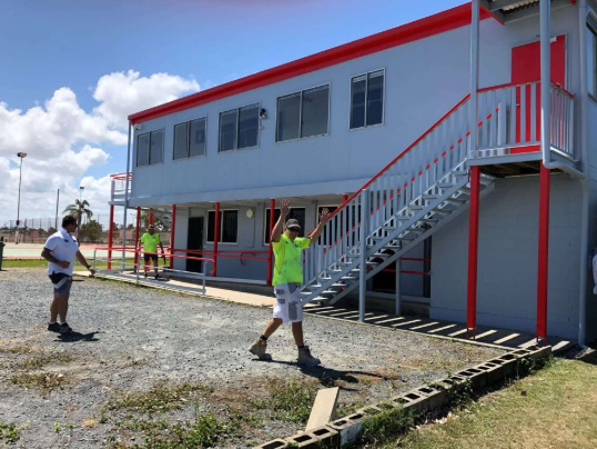 A man in a neon green shirt is standing in front of a building with stairs.
