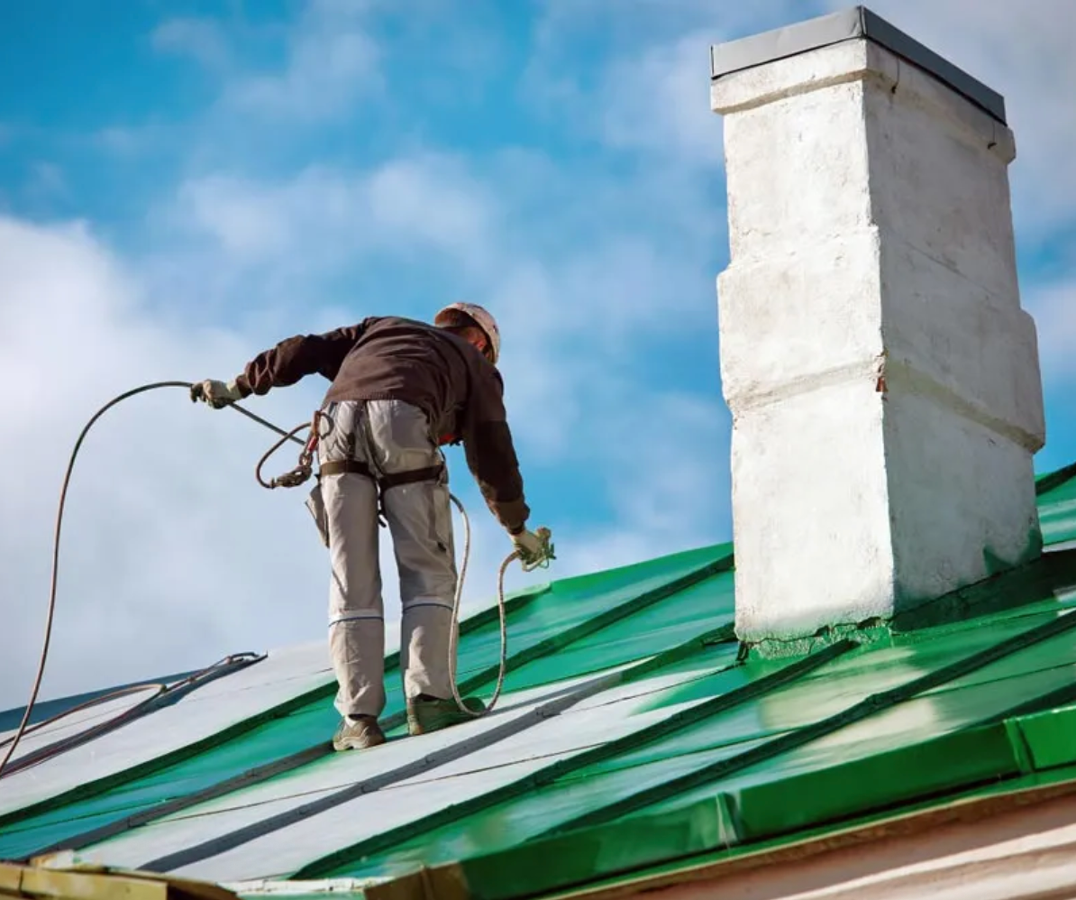 Man with harness spraying green paint onto a roof, showcasing professional house painting services.