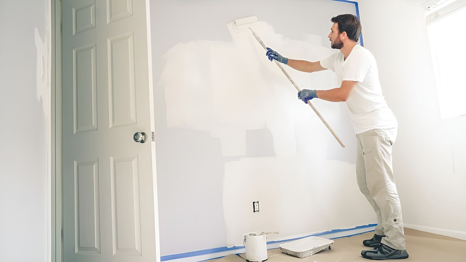 Man Painting A White Wall With A Roller