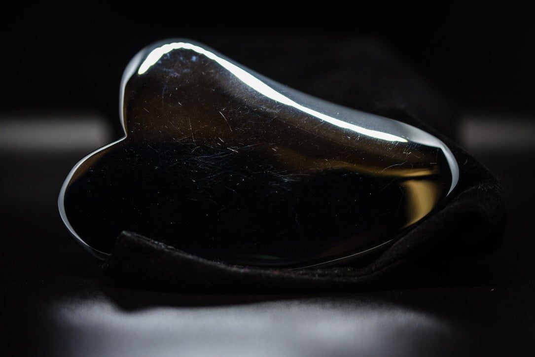 A silver heart shaped object is sitting on a black surface