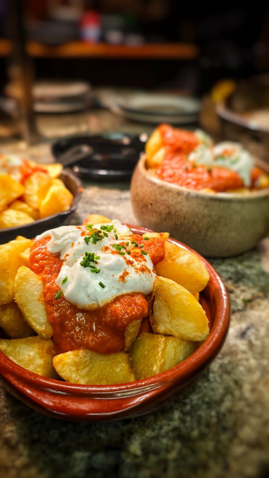 A bowl of potatoes with sauce and sour cream on a table.