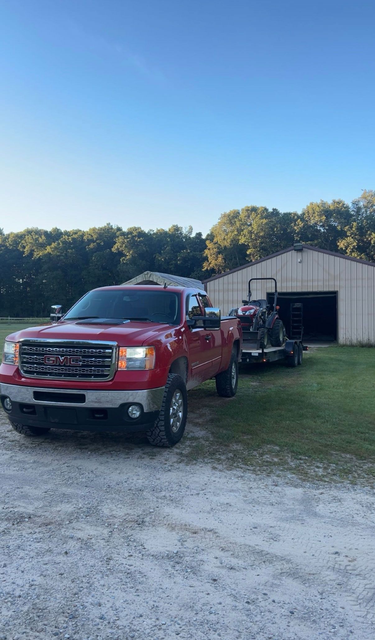 Red pickup truck towing a trailer near a barn on a sunny day.