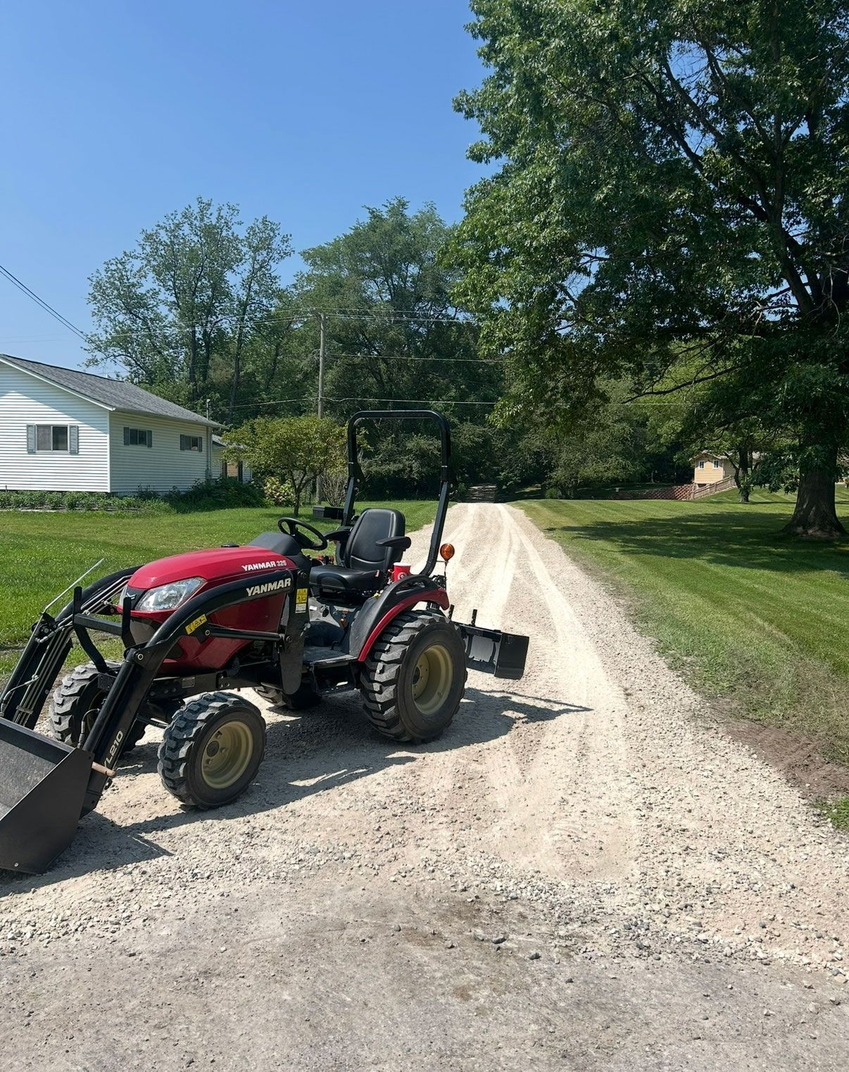 Red tractor on a gravel road, likely for maintenance, in a rural setting.