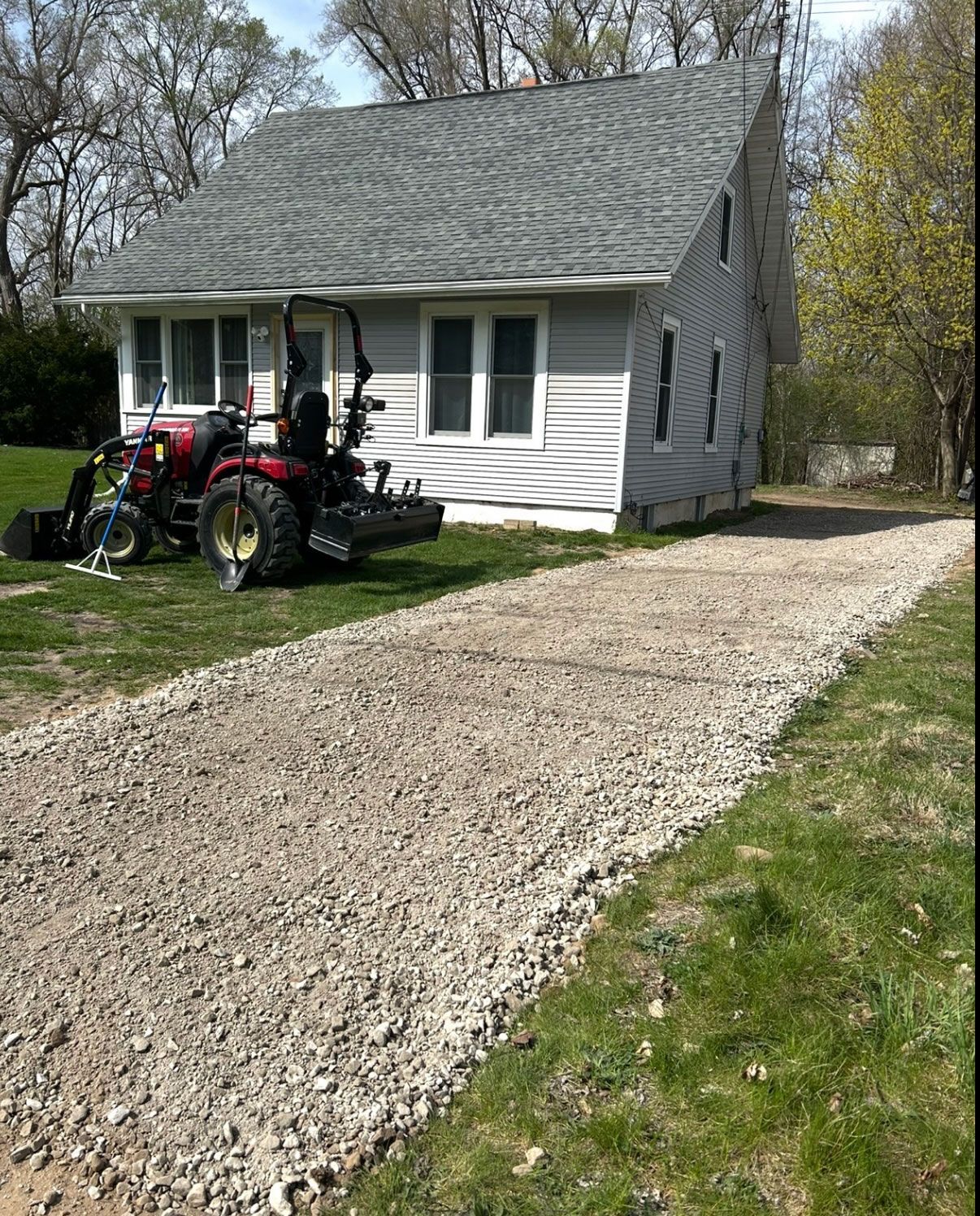 Gravel driveway leading to a light gray house. A tractor is parked in the yard.