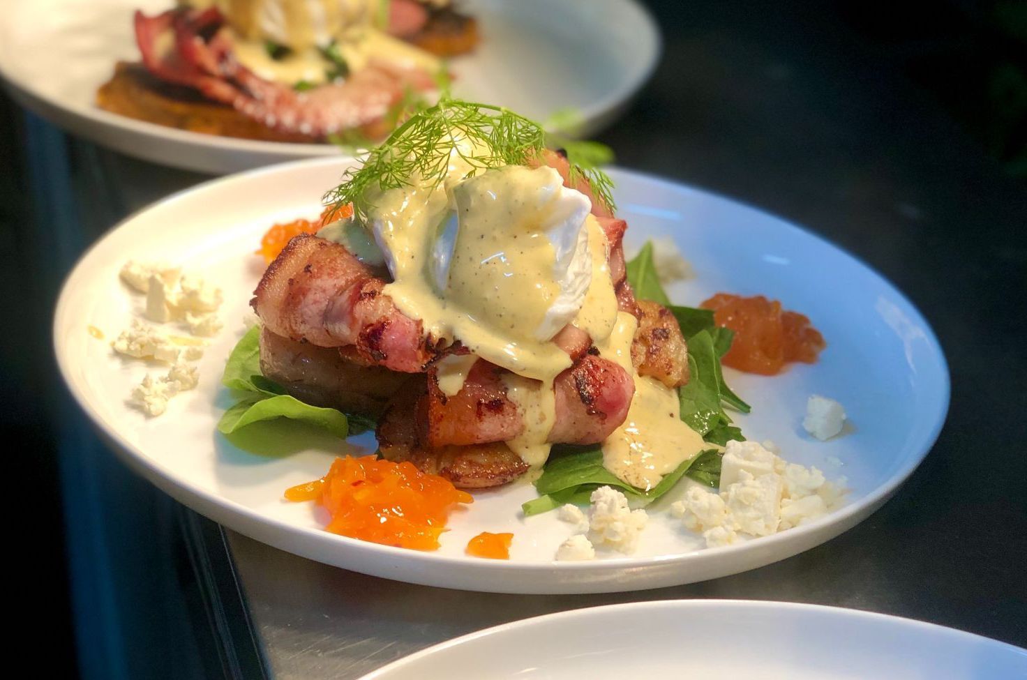 A Plate of Eggs Benedict With Bacon, Hollandaise, Greens, and Orange Garnish — Flour in Yeppoon, QLD