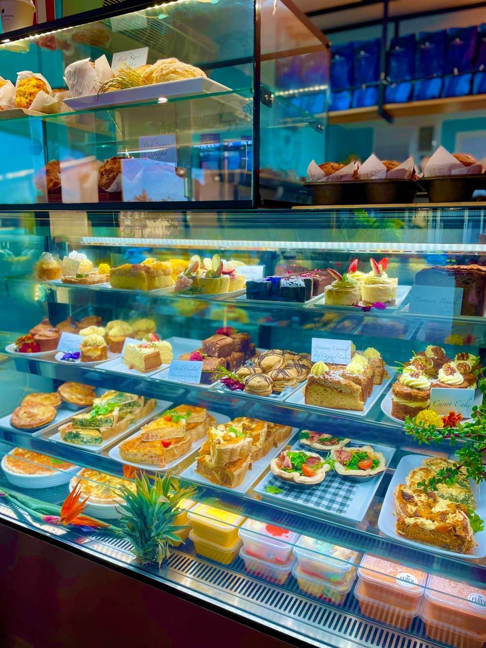 A Glass Display Case Filled With Pastries, Cakes, and Sandwiches in a Cafe Setting With Teal Accents — Flour in Yeppoon, QLD
