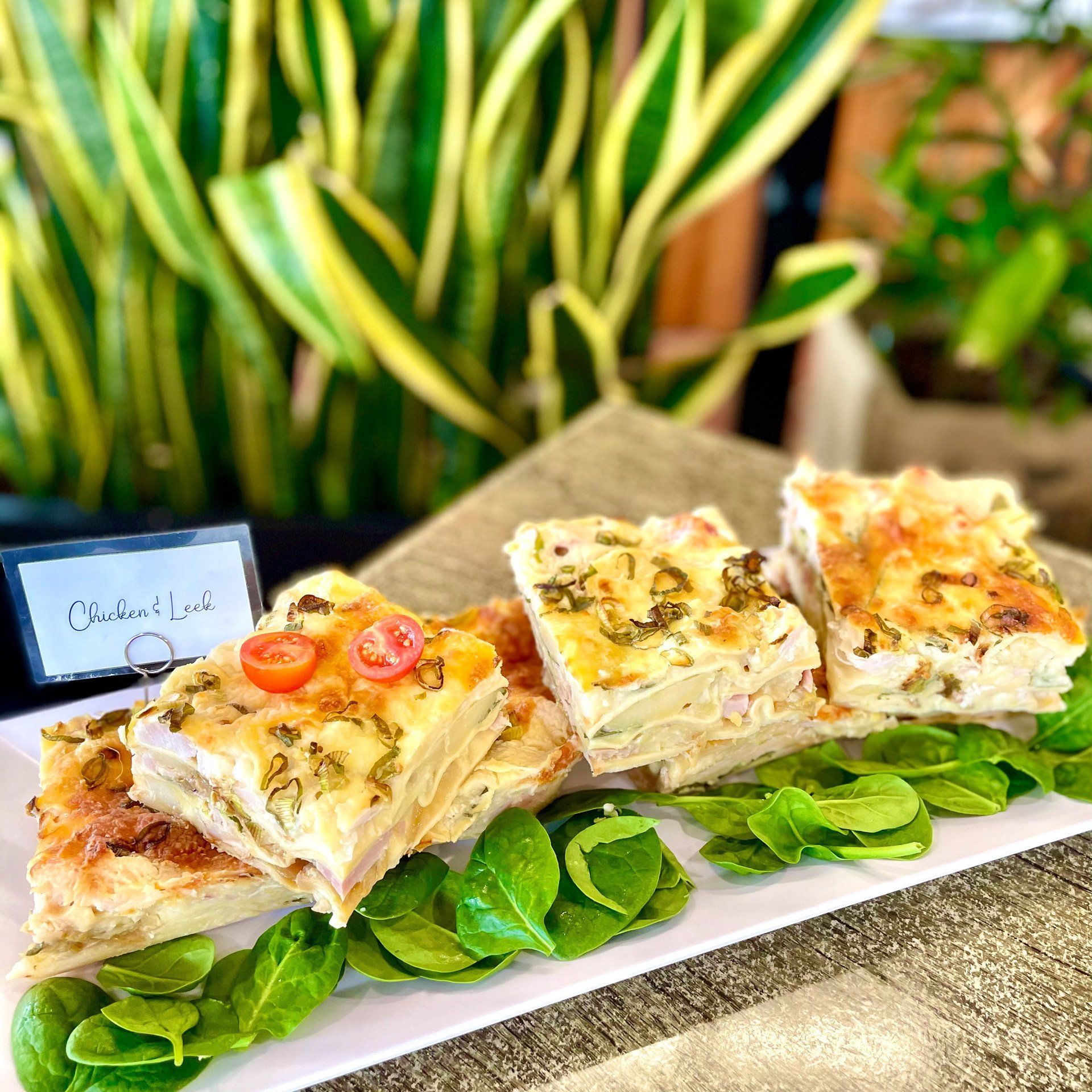 A Potato Casserole Slices With Spinach Garnish, on a Plate, With a Plant Background — Flour in Yeppoon, QLD