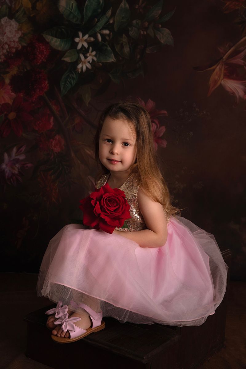 A little girl in a pink dress is holding a red rose.