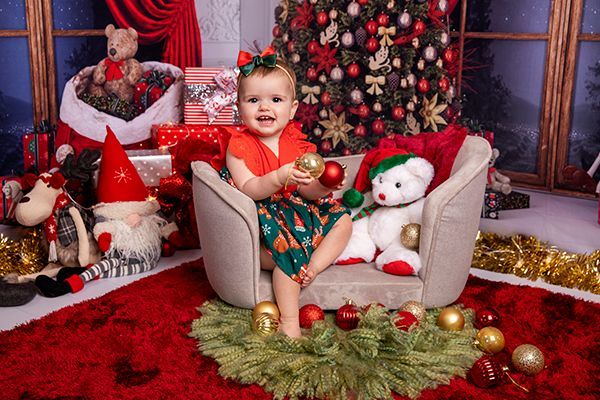 A baby girl is sitting in a chair holding a christmas ball.