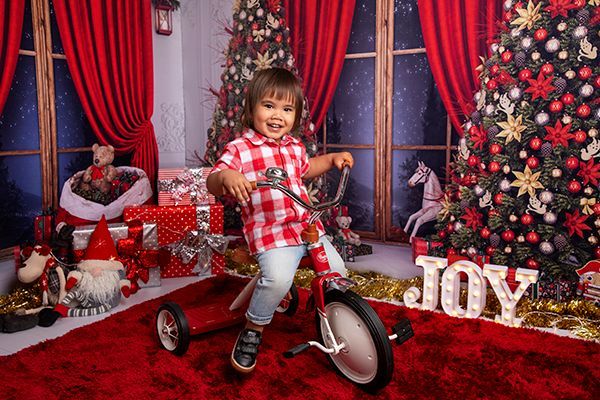 A little boy is riding a tricycle in front of a christmas tree.