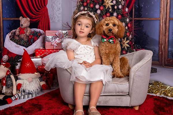 A little girl is sitting on a couch with a dog in front of a christmas tree.