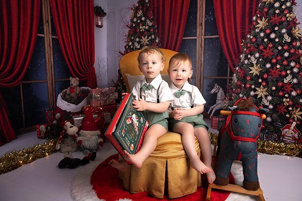 Two little boys are sitting in a chair in front of a christmas tree.