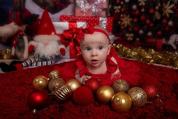 A baby is laying on a red blanket surrounded by christmas decorations.