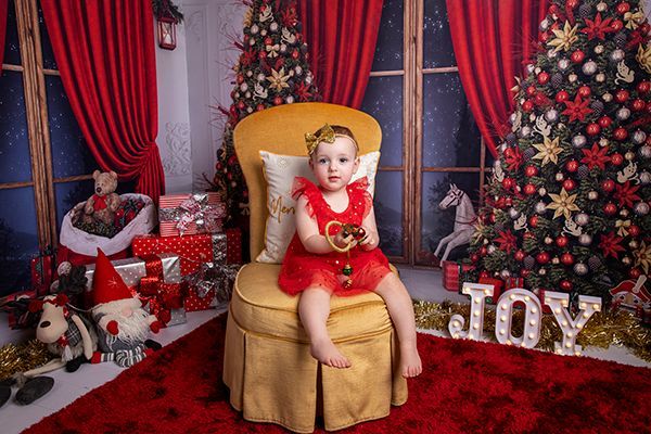 A little girl is sitting in a chair in front of a christmas tree.