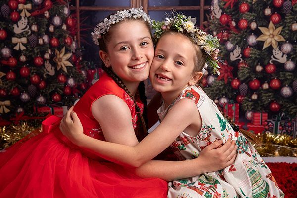 Two little girls are hugging each other in front of a christmas tree.