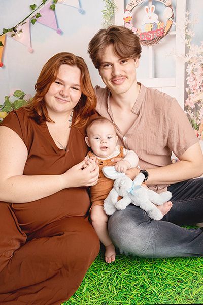 A pregnant woman , a man and a baby are posing for a picture.