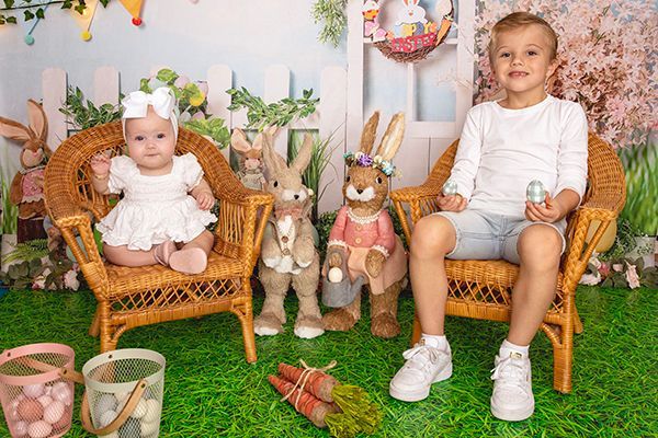 A boy and a baby are sitting in wicker chairs with easter bunny figurines.
