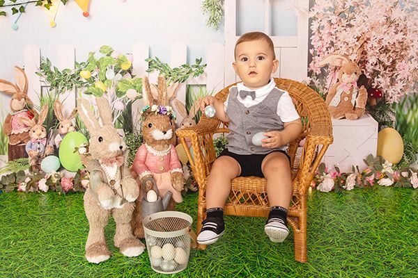 A baby is sitting in a wicker chair surrounded by stuffed rabbits.