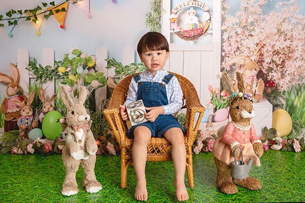 A little boy is sitting in a chair surrounded by stuffed rabbits.