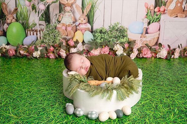 A newborn baby is sleeping in a bowl surrounded by easter eggs and flowers.